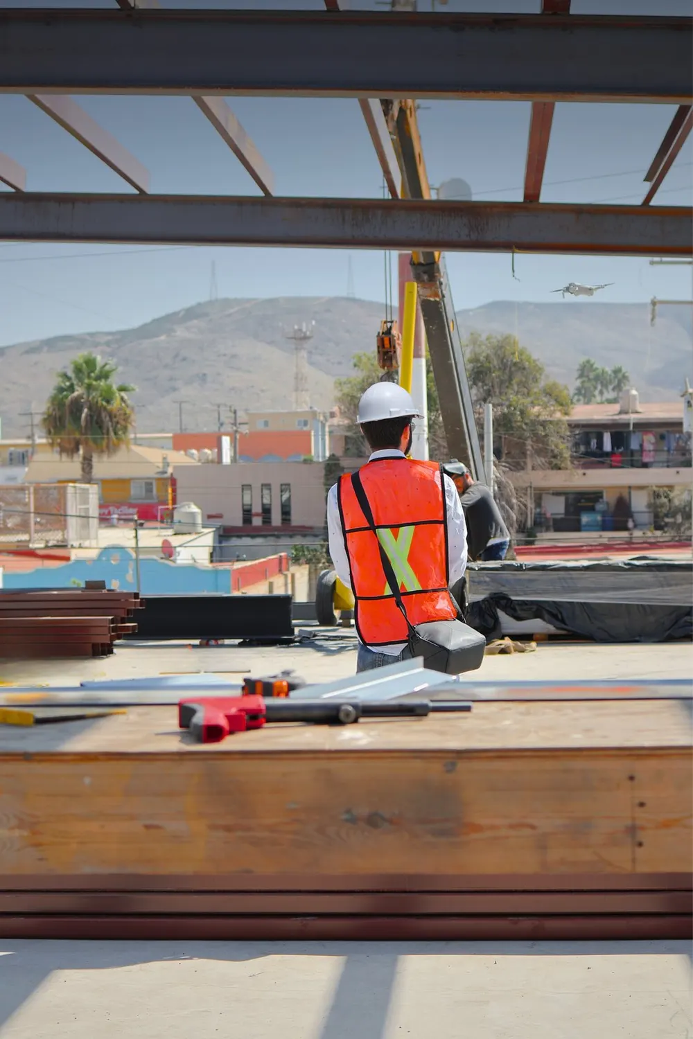 Trabajador con chaleco reflejante en una estructura metálica, con la ciudad al fondo
